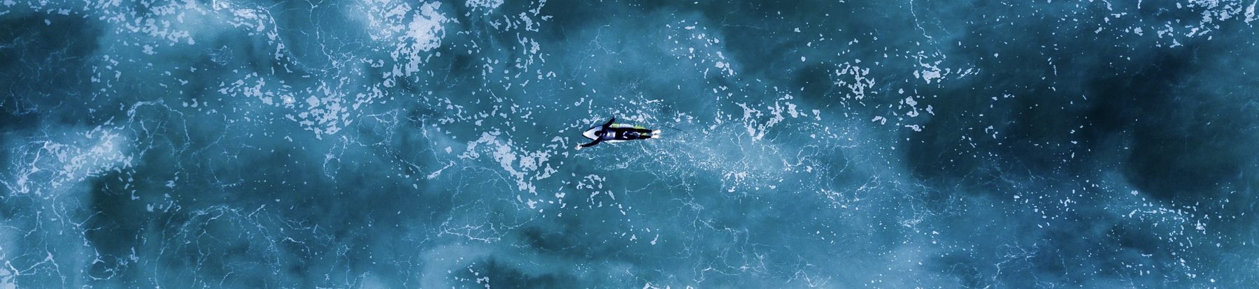 Aerial view of a surfer paddling through the ocean.